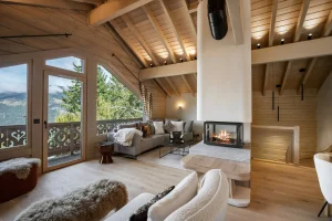 Lounge under light timber beams with a central fireplace and a carved-balustrade balcony at Chalet Églantine in Courchevel La Tania