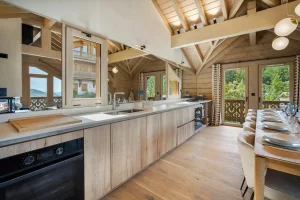 Open kitchen with a light worktop, a built-in oven and a laid dining room at Chalet Églantine in Courchevel La Tania