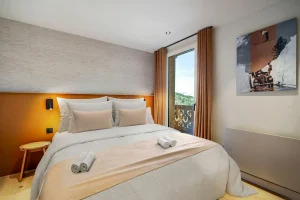Double bedroom with an orange headboard, ochre curtains and a French door onto the balcony at Chalet Églantine in Courchevel La Tania