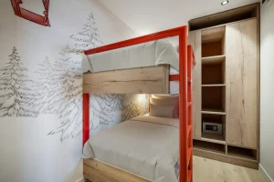 Bedroom with wooden and red metal bunk beds, a fir-tree mural and a wardrobe with a safe at Chalet Églantine in Courchevel La Tania