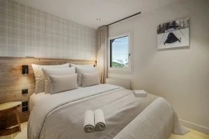 Double bedroom with a grey linen bed, check wallpaper and a window onto the mountain at Chalet Églantine in Courchevel La Tania
