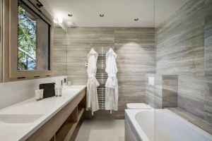 Bathroom with a double washbasin, a bathtub and a window onto the fir trees at Chalet Églantine in Courchevel La Tania