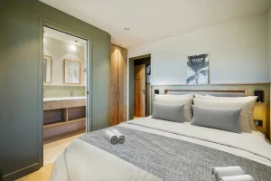 Double bedroom with an upholstered headboard, sage-green walls and an en-suite shower room at Chalet Églantine in Courchevel La Tania