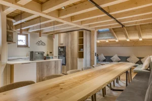 Large solid wood table and open kitchen under exposed beams at Chalet Épicéa in Les Saisies