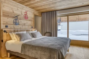 Bedroom with a large bed, a wooden headboard and a glazed door onto the snow at Chalet Épicéa in Les Saisies