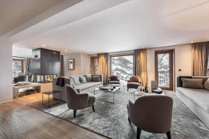 Living area with a lounge, grey armchairs and a central fireplace opening onto the large windows at Chalet Merlin in Saint-Martin-de-Belleville