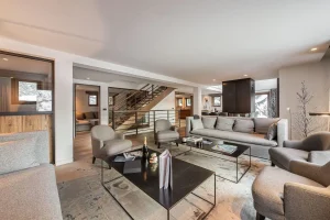 Lounge with sofas, armchairs and a metal coffee table, with the staircase beyond at Chalet Merlin in Saint-Martin-de-Belleville