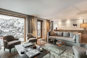 Lounge with a large picture window onto the mountains and a grey sofa at Chalet Merlin in Saint-Martin-de-Belleville
