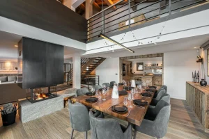 Dining room with a laid timber table, a central fireplace and a mezzanine at Chalet Merlin in Saint-Martin-de-Belleville