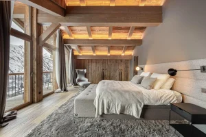 Master suite under exposed beams with a double bed and picture windows onto the mountains at Chalet Merlin in Saint-Martin-de-Belleville