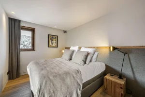 Double bedroom with a bed, an articulated lamp and a window onto the mountains at Chalet Merlin in Saint-Martin-de-Belleville