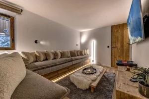 Cinema room with a long curved sofa, a wall-mounted screen and a sheepskin pouffe