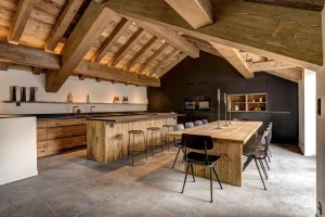 Open kitchen with a timber island, black chairs and a dining table beneath the roof frame