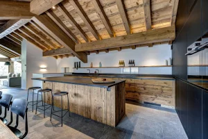 Kitchen island with bar stools and a dark cooking wall, with the dining table beyond