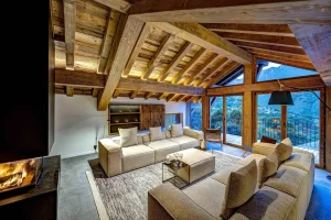 Chalet Villette's open-plan living area with cream sofas under exposed roof beams, with a view of the valley