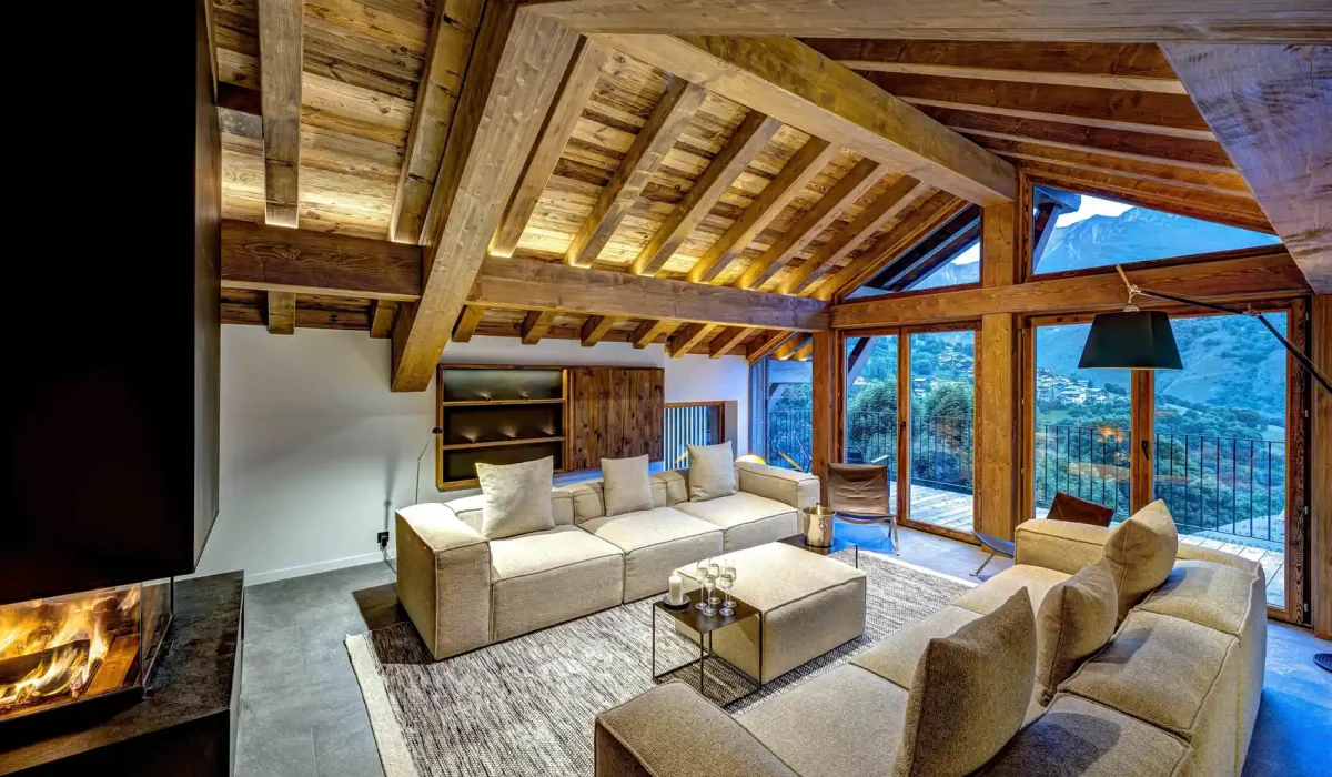 Chalet Villette's open-plan living area with cream sofas under exposed roof beams, with a view of the valley